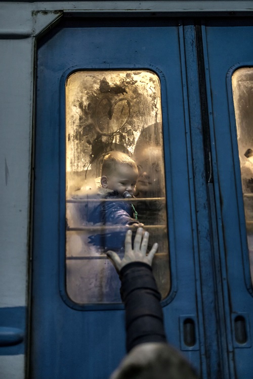 En man sträcker ut sin hand mot ett litet barn på andra sidan en tågdörr.